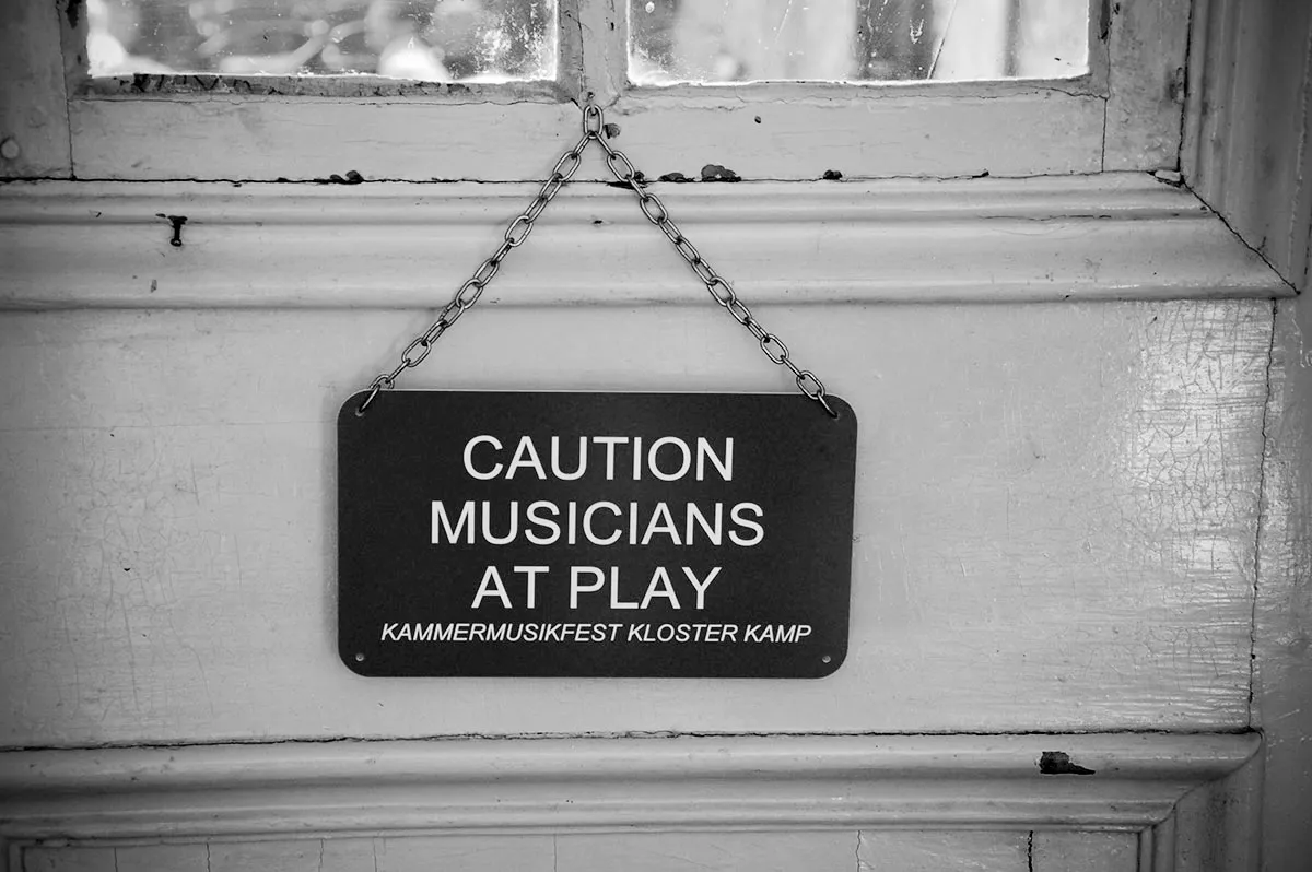 Vor einer alten Tür mit Glaseinsätzen hängt ein Schild mit der Aufschrift 'Caution Musicians at play'